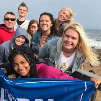 Students holding a GVSU flag by the ocean